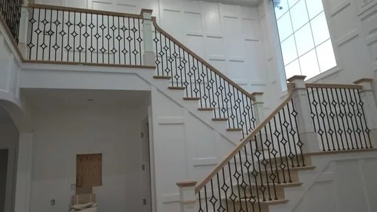Custom stair railing installation on main staircase with detailed white paneling.