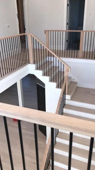 Modern stair railing installation on upper landing with wood handrail and black balusters.