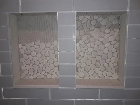 Shower tile installation detail showing dual recessed niches with pebble-stone tile.