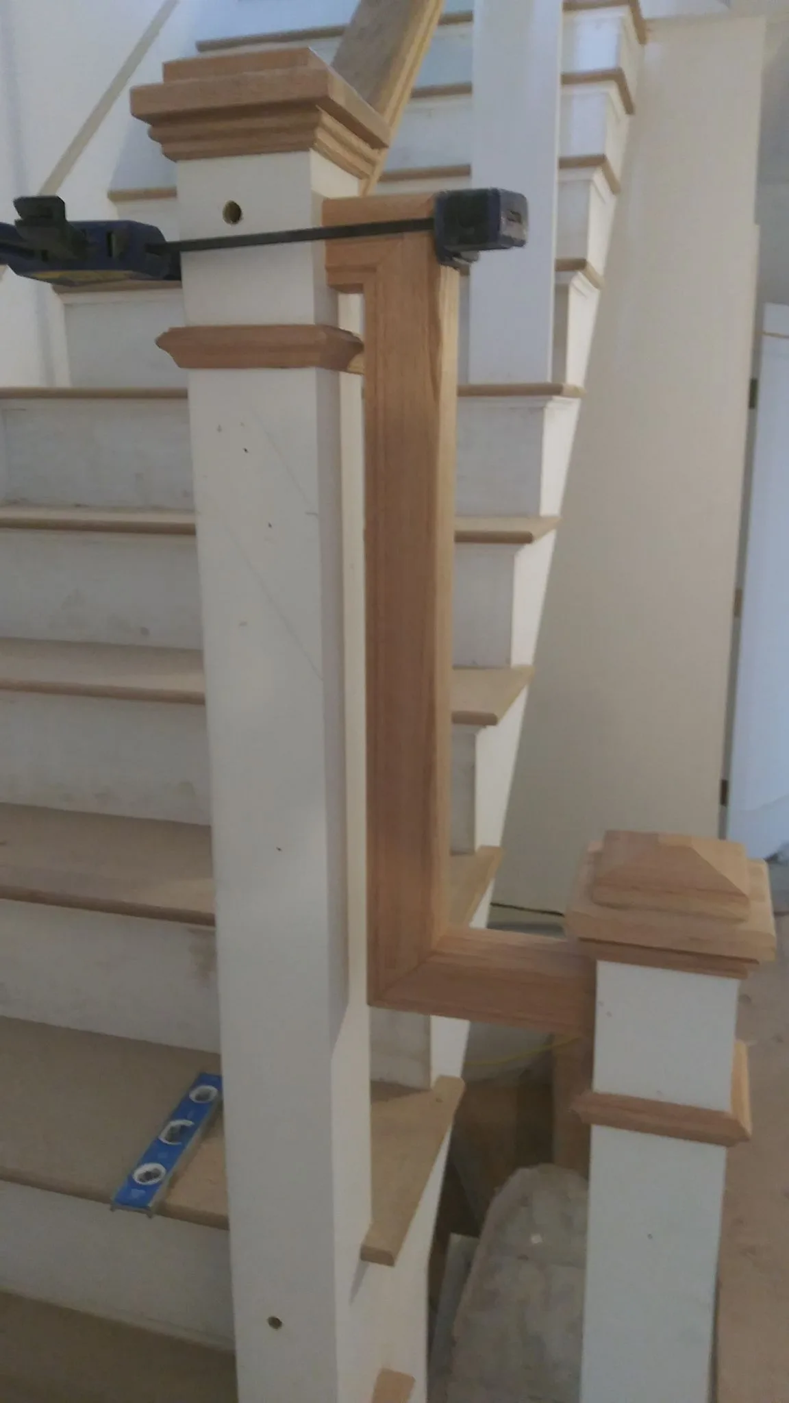 A detailed view of a custom staircase handrail transition being clamped to a white newel post during a home renovation.