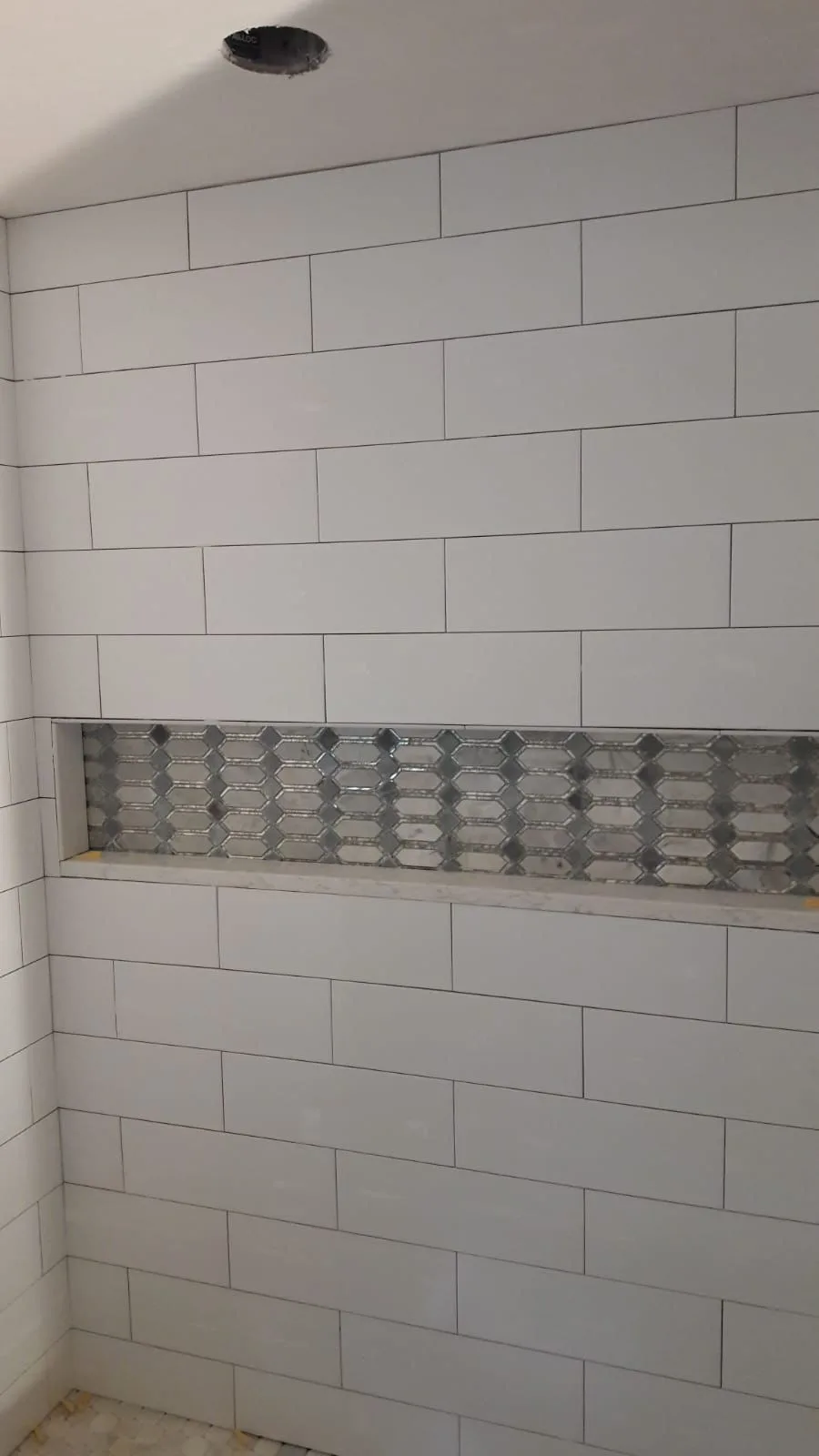 A custom shower tile installation featuring white subway tiles and a horizontal recessed niche with geometric mosaic accent tiles.