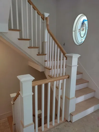 Side view of a custom staircase design highlighting the white newel posts, oak handrail, and oval window.