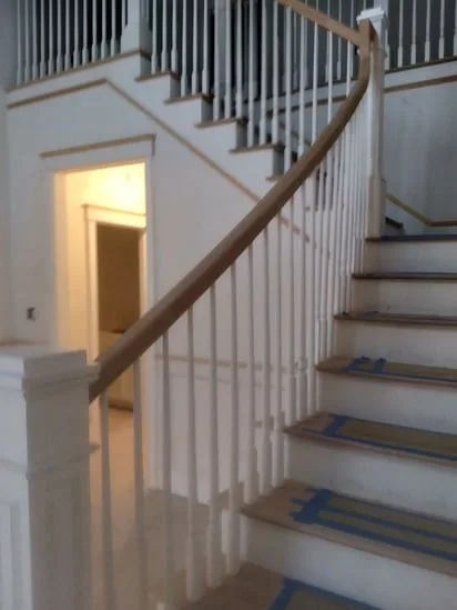 A completed residential staircase railing installation featuring natural wood handrails and white balusters.