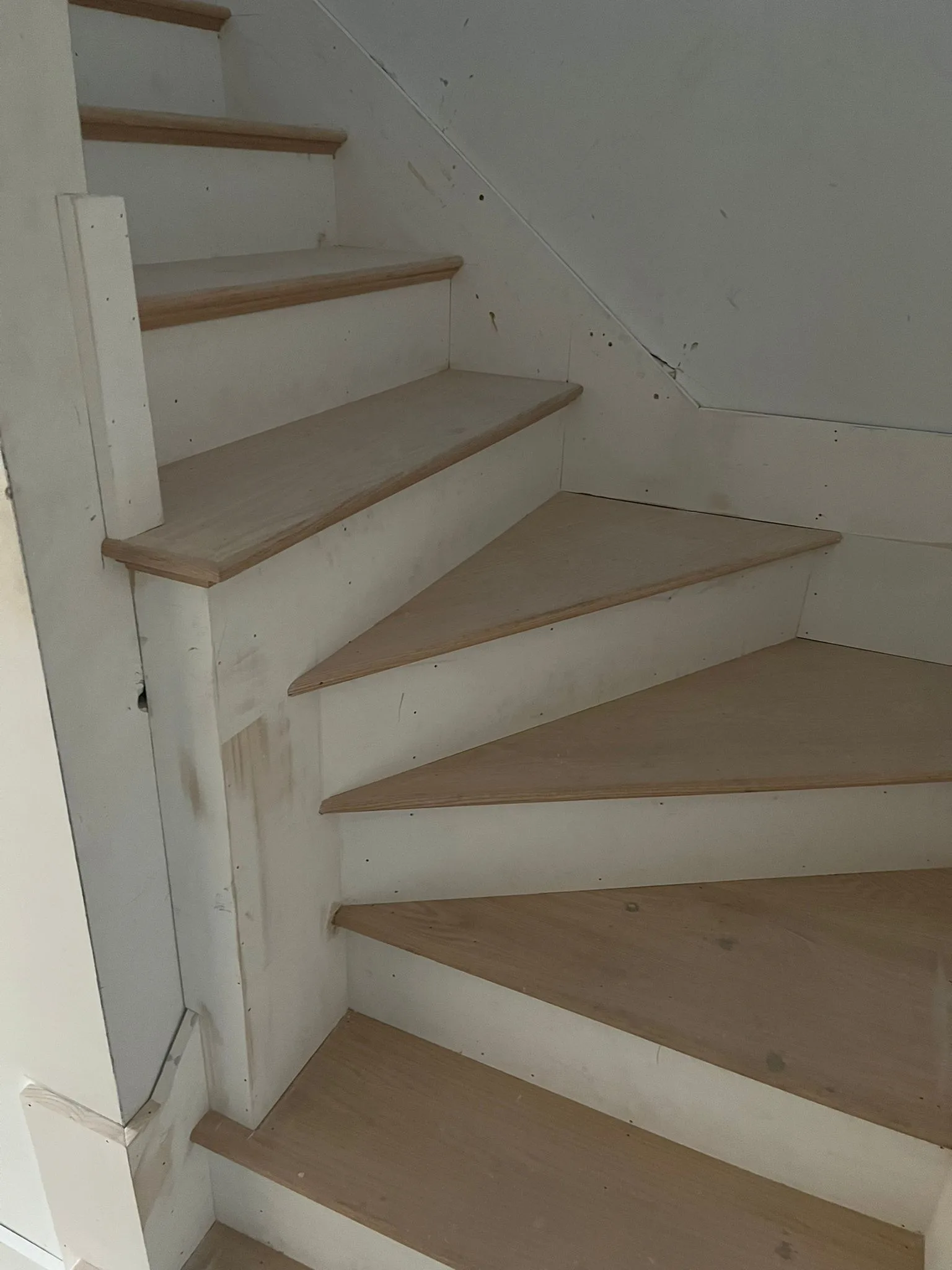 An interior shot of custom curved stair carpentry with light wood treads and painted white risers under construction, showcasing the precise fitment.