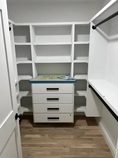 Custom walk-in closet featuring white built-in shelving, a central floating drawer unit, and black hanging rods.