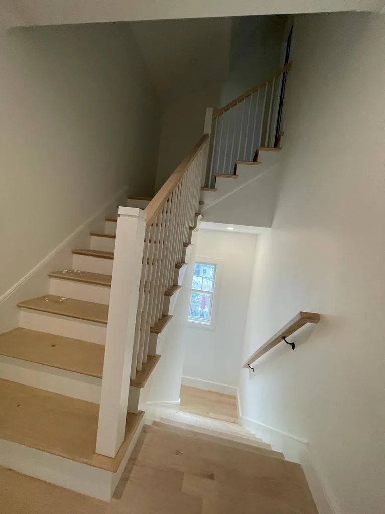 A freshly completed finished interior stair carpentry project, featuring light wood treads and a handrail with white painted balusters.